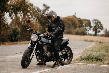 motorrijder typt bericht in smartphone met handschoenen aan, aangepaste motorfiets caféracer.