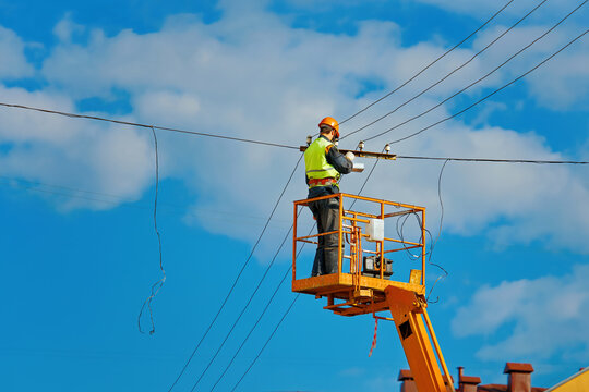 Worker On Cherry Picker Install Led Lantern On Electric Wires At Height. Man In Lift Bucket Upgrade Street Lights, Install Led Panel Outdoor. Improving Outdoor Street Lights On Energy Efficient Light