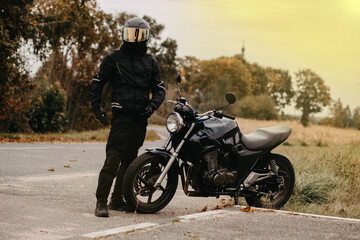 Obraz premium motorcyclist with motorcycle retro cafe racer on autumn road in uniform and helmet. the concept of the end of the motorcycle season.