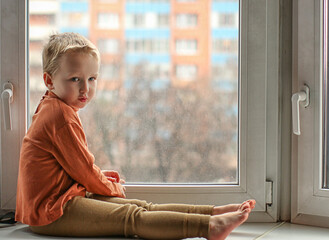 a boy in an orange shirt sits on the window