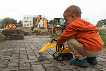 Child with excavator near construction site, dreams to be an engineer. Little builder. Education,...