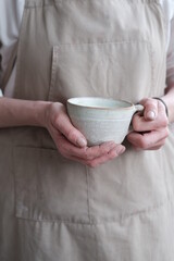 Women in the apron holding handmade clay and turquoise cup of tea. Clay workshop