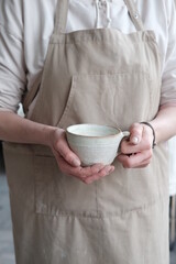 Women in the apron holding handmade clay and turquoise cup of tea. Clay workshop