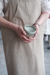 Women in the apron holding handmade clay and turquoise cup of tea. Clay workshop