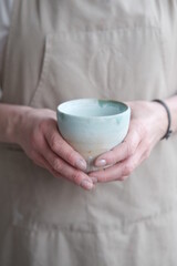 Women in the apron holding handmade clay and turquoise cup of tea. Clay workshop