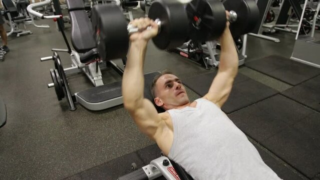 Sporty young man does dumbbell presses on bench at an gym. Chest workout