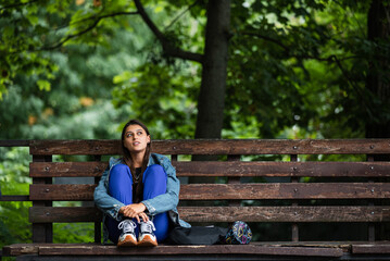 Pensive woman sitting on a bench in a park looking away
