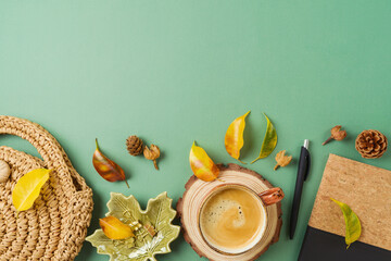 Coffee cup, planner, bag and autumn leaves on green background. Stylish boho home office table. Top...