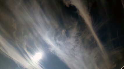 High cirrus clouds in the sky. White oblong translucent clouds hang against a light blue sky. They...