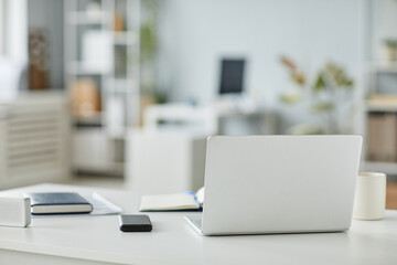 Minimal background image of opened laptop at workplace in office interior in white and grey tones, copy space