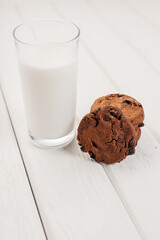 A glass of milk with chocolate chip cookies on a light table.