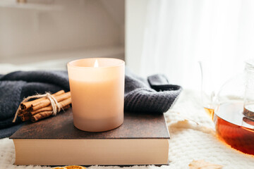 Autumn mood, a burning candle, a book and a kettle of hot tea on a cozy plaid. Atmospheric,...