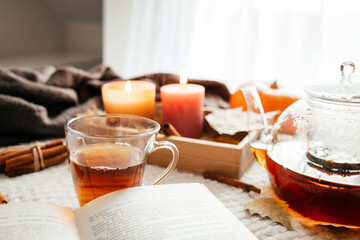 Autumn mood, a burning candle, a book and a kettle of hot tea on a cozy plaid. Atmospheric,...
