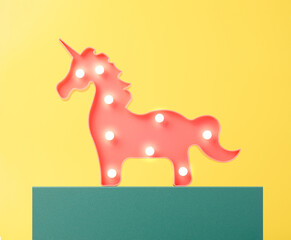 Pink unicorn with lightbulbs lit standing on a teal stand. Energy fantasy minimal concept