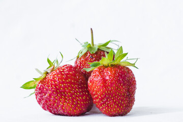 Three ripe strawberries with strawberry leaf, isolated on a white fabric background. Bunch of strawberries. Healthy eating and harvesting farm organic food concept