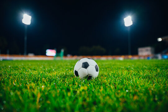 Football ball on green grass on soccer stadium in night. Sport photo, black edit space