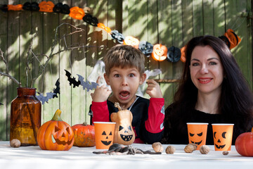 Portrait mother and son on sunny autumn day against background of old wooden wall. Family mother and son are preparing for Halloween, decorating yard of their house with festive decorations