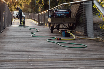 municipal employee cleaning a wooden bridge with a pressure washing machine