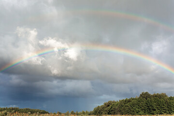 Double rainbow over Lithuanian meadows and forest at cloudy day