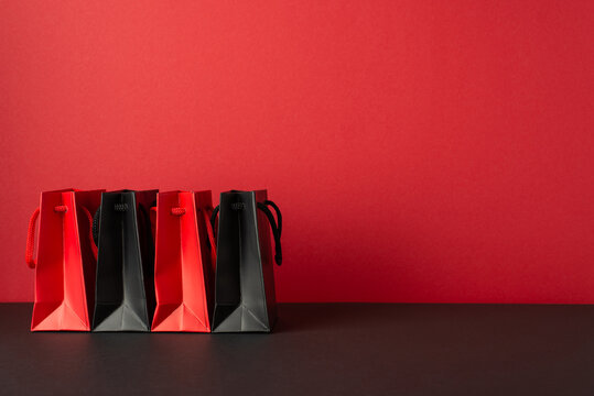 Black friday shopping concept. Photo of red and black paper bags on black tabletop red wall background