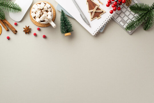 Winter concept. Top view photo of keyboard computer mouse notepads wood fir ornament mug of cocoa with marshmallow mistletoe pine branches and cinnamon stick on isolated grey background with copyspace
