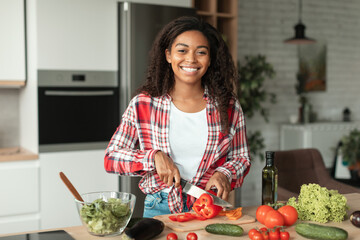Glad pretty millennial african american female cutting organic vegetables and looking at camera,...