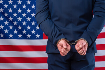 Business man in suit jacket handcuffed with united states flag in background. Political and...