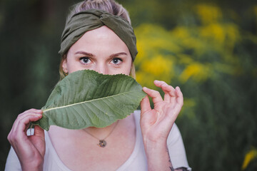 closeup of a young healthy alternative & spiritual looking woman holding a green plant leaf half in...