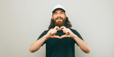 Portrait of cheerful young bearded man showing heart gesture with hands.