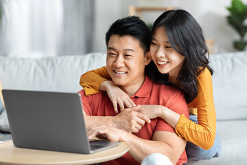 Loving chinese man and woman using computer together at home
