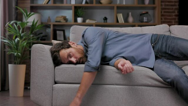 Tired man collapses on the couch, feeling apathetic. Feeling depressed, lack of motivation, sadness, boredom. Exhausted, he collapses on the couch from the stress. Burnout