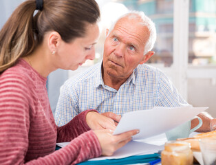 Sad young woman and father with financial documents at home interior