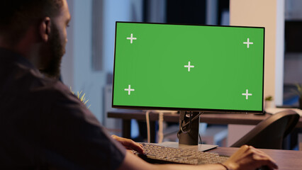 African american man looking at computer with greenscreen, analyzing isolated display on desktop...