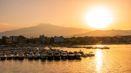 Fototapeta premium picturesque sunrise or sunset in a sea port with a gulf dock pier with tour boats and a town with cloudy sky on background of a seashore landscape