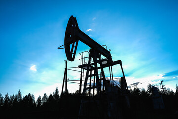An abandoned oil or gas rocking machine against a blue sky, exhausted resource. A clogged field of...