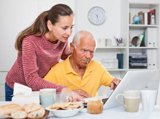 Portrait of father and adult daughter at table using laptop together