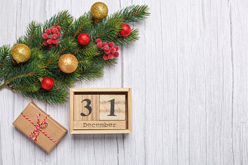 christmas tree branch with toys and gifts and wooden calendar december 31 on a wooden background