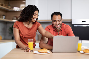 Fototapeta na wymiar Glad millennial black family enjoy breakfast in morning together, lady pointing finger at laptop