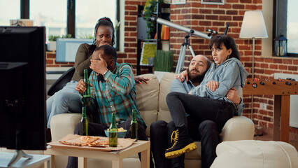 Terrified people watching scary movie on tv channel, being frightened of jump scare at chill hangout. Getting afraid and screaming while they watch horror thriller film. Handheld shot.