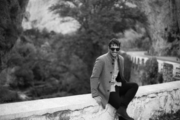 Chico caucásico sentado en muro al borde de la carretera. Foto en blanco y negro.