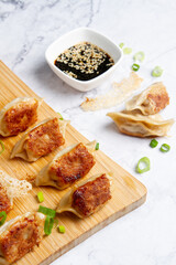 dumplings or gyosas are on a wooden board, another dumpling is on the table with soy sauce
