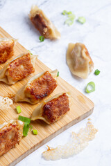 dumplings or gyosas are on a wooden board, two more dumpling are on the table 