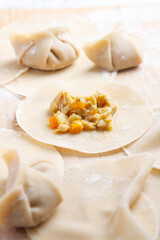 A wooden surface , showcasing dough pieces in the process of being crafted into dumplings. Several pieces are folded and sealed, while one remains open, revealing a vibrant vegetable filling