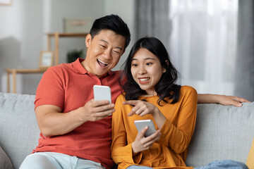 Cheerful chinese spouses using smartphones, home interior