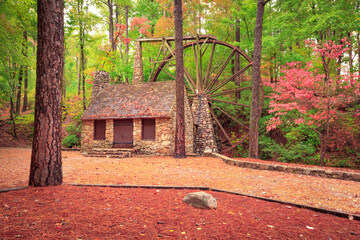 Stone building with chimney and mill wheel in forest during autumn