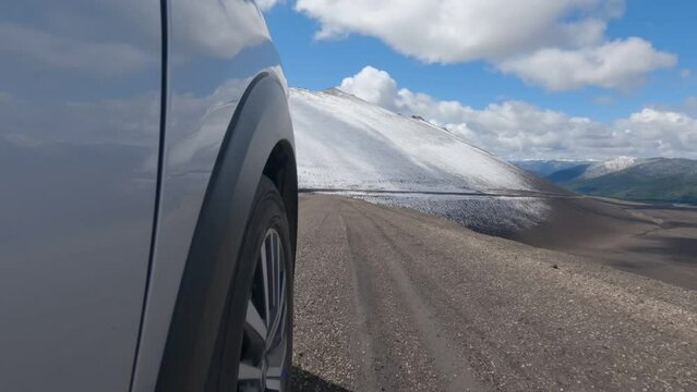 Vista a nivel del suelo de c&aacute;mara de acci&oacute;n. Camioneta recorriendo un camino de ripio con monta&ntilde;as nevadas, cielo azul y nubes en el sur de chile.