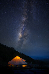 Tent Camping glows on mountain peak with milky way in starry night background