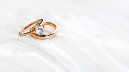 Pair of golden wedding rings on white textile background with copy space. Engagement ring with diamond on fabric backdrop. Symbol of love and marriage. - obrazy, fototapety, plakaty
