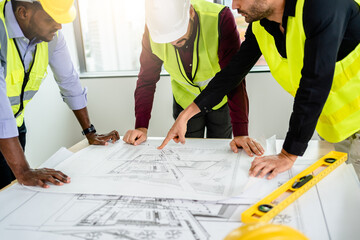 Team of Engineers diverse in safety suite discussing draft blueprints and on the desk at the...