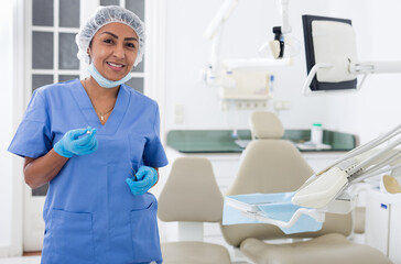 Confident professional dentist woman posing in dental clinic, looking with smile at camera
